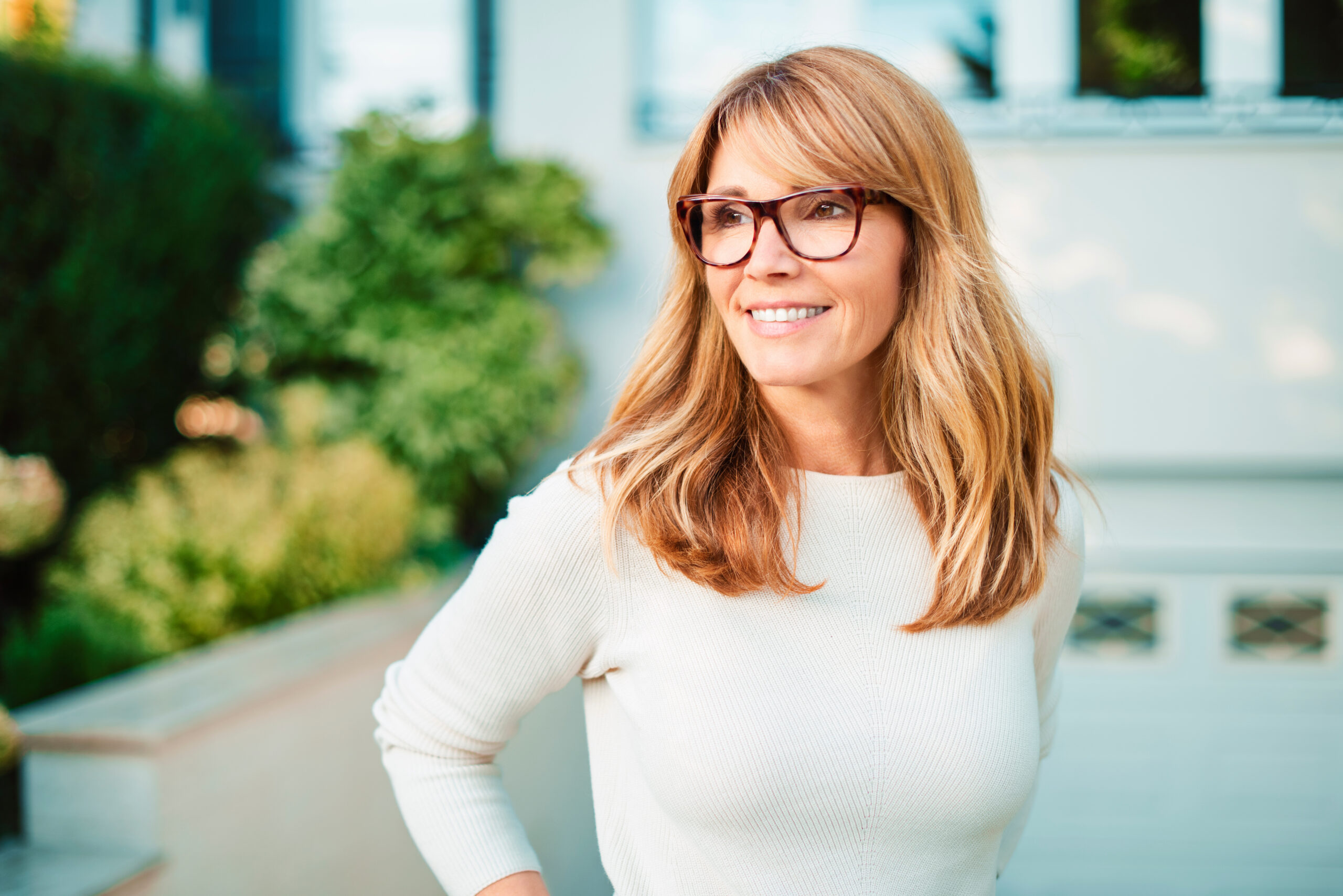 Attractive middle aged woman outdoor portrait Portrait shot of confident mature woman standing in front yard of home while looking at camera and smiling.